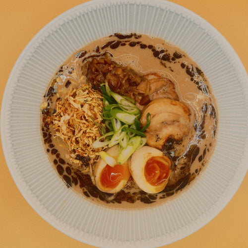 Creamy Chicken & Mushroom Ramen from above, with chicken chashu, mushroom ragu, yuzu cabbage, spring onion and a halved egg in a creamy broth swirled with black garlic butter