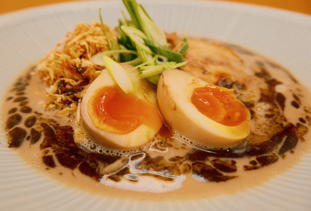 Close-up of Creamy Chicken & Mushroom Ramen, with a halved egg and yuzu cabbage over creamy chicken broth and black garlic butter