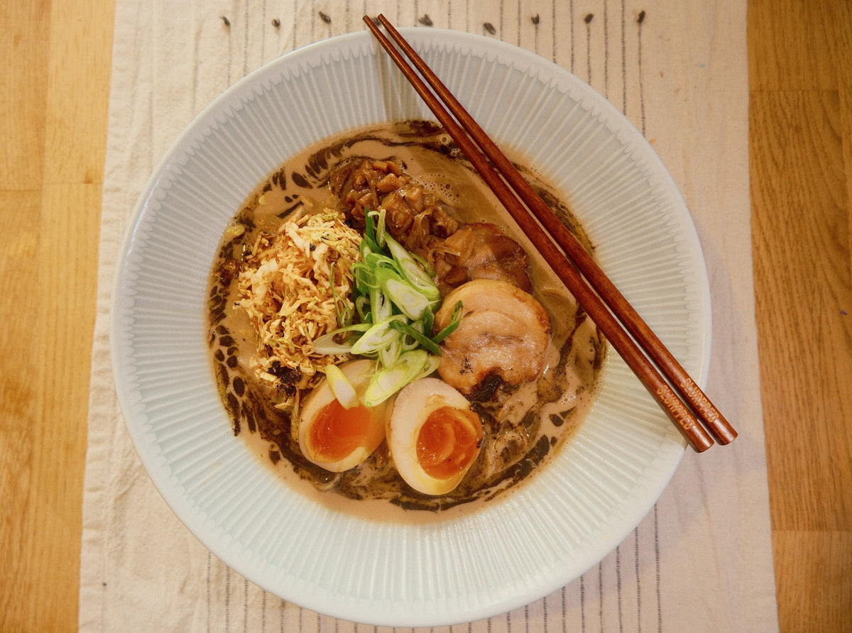A bowl of Creamy Chicken & Mushroom Ramen on a laid wooden table with chopsticks