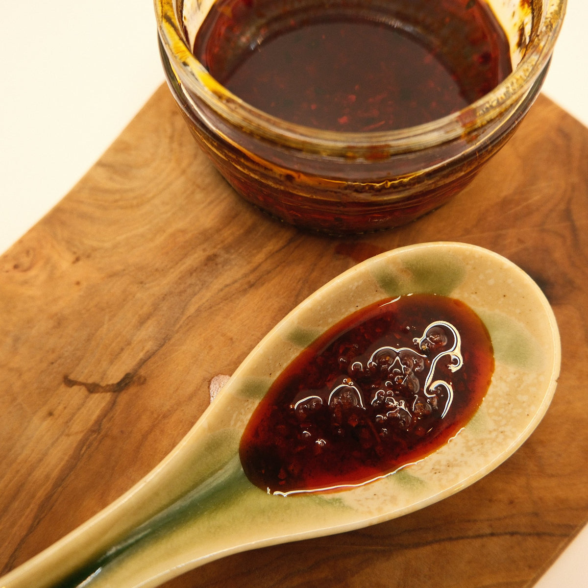 A spoonful of house rayu chilli oil on a wooden board beside the jar